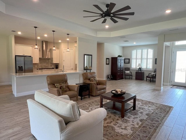 living room featuring ceiling fan, light wood-type flooring, sink, and a tray ceiling