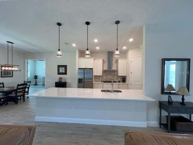 kitchen featuring wall chimney range hood, decorative light fixtures, stainless steel fridge, and white cabinets