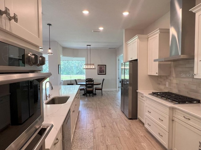 kitchen with wall chimney exhaust hood, sink, white cabinetry, decorative light fixtures, and appliances with stainless steel finishes