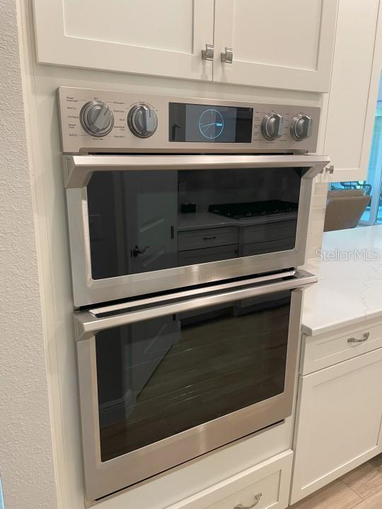 room details with white cabinetry, light stone countertops, double oven, and light wood-type flooring