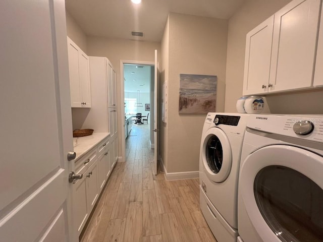 laundry area with washing machine and dryer, cabinets, and light wood-type flooring