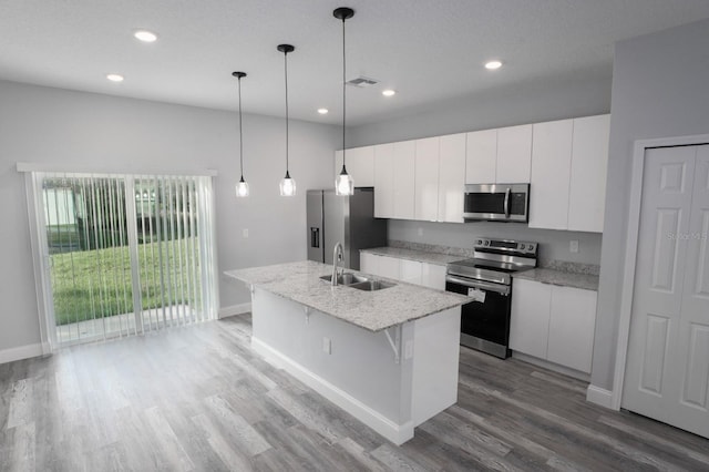 kitchen featuring appliances with stainless steel finishes, sink, decorative light fixtures, wood-type flooring, and a center island with sink