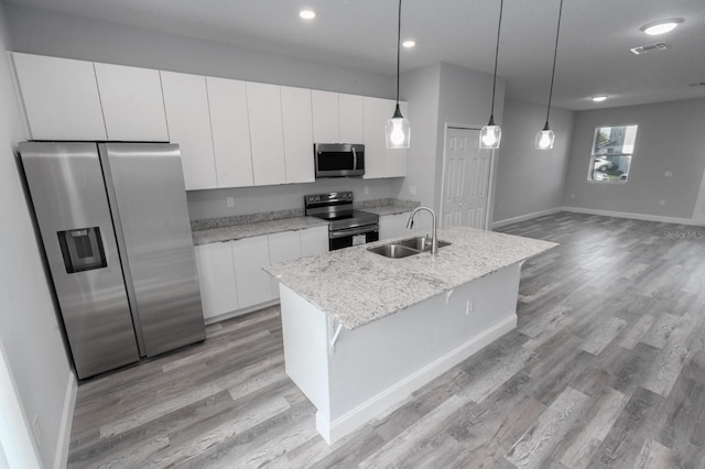 kitchen with decorative light fixtures, appliances with stainless steel finishes, light hardwood / wood-style flooring, a center island with sink, and white cabinets