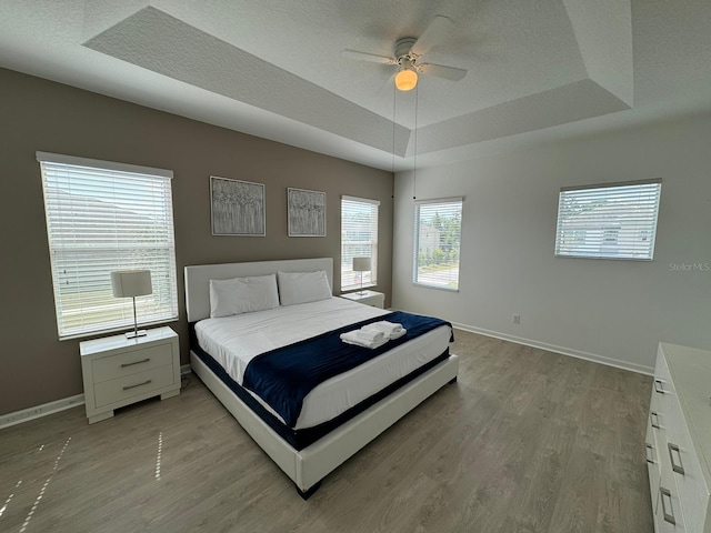 bedroom with hardwood / wood-style floors, ceiling fan, and a tray ceiling