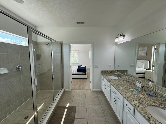 bathroom with vanity with extensive cabinet space, a textured ceiling, an enclosed shower, tile floors, and dual sinks