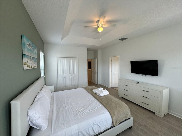 bedroom with a closet, ceiling fan, a textured ceiling, light hardwood / wood-style floors, and a raised ceiling