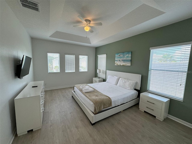 bedroom featuring light wood-type flooring, ceiling fan, a textured ceiling, and a tray ceiling