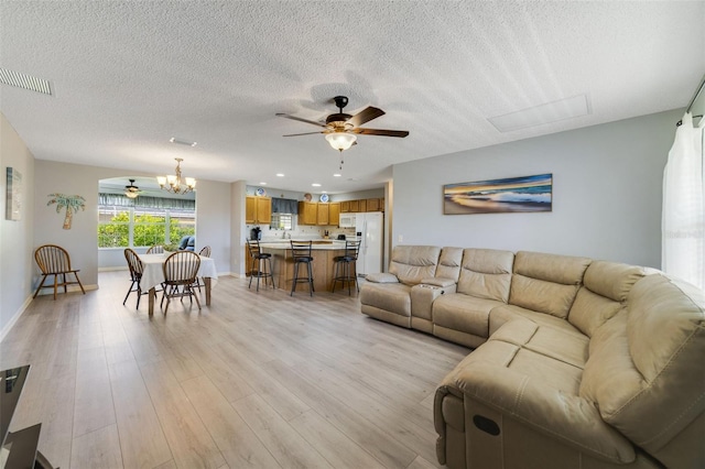 living room featuring ceiling fan with notable chandelier, light hardwood / wood-style flooring, and a textured ceiling