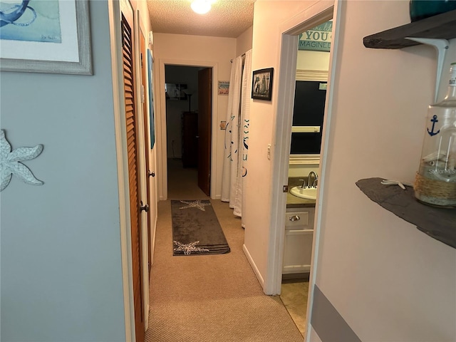 corridor with a textured ceiling, a sink, and light colored carpet