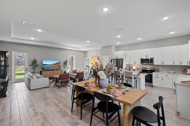 dining space with light hardwood / wood-style floors and a raised ceiling