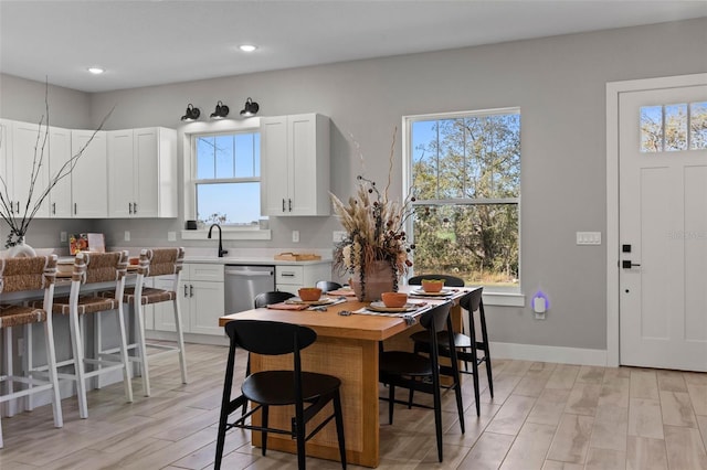 kitchen featuring white cabinetry, dishwasher, sink, a kitchen breakfast bar, and light hardwood / wood-style flooring