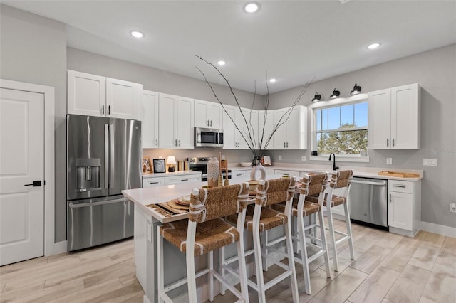 kitchen with appliances with stainless steel finishes, light hardwood / wood-style flooring, a center island, white cabinetry, and a breakfast bar area