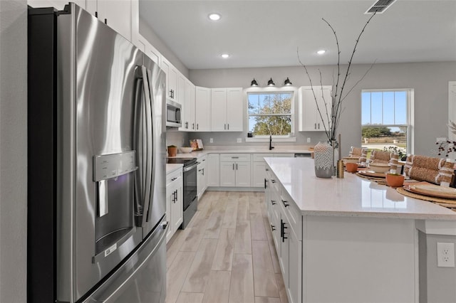 kitchen with a center island, white cabinets, sink, light stone counters, and stainless steel appliances