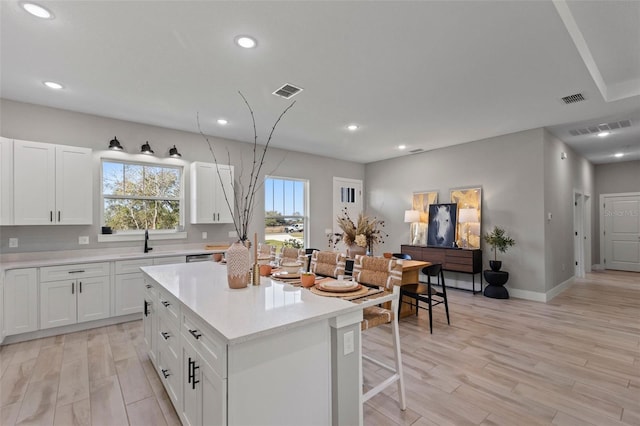 kitchen with light hardwood / wood-style floors, a kitchen island, white cabinetry, and sink