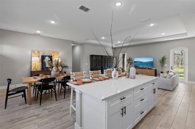 kitchen featuring a kitchen breakfast bar, a center island, white cabinetry, and a tray ceiling