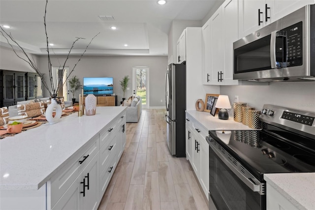 kitchen featuring light stone countertops, stainless steel appliances, a tray ceiling, white cabinets, and light wood-type flooring