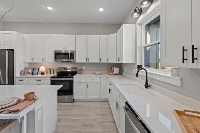 kitchen featuring light stone counters, stainless steel appliances, sink, light hardwood / wood-style flooring, and white cabinets