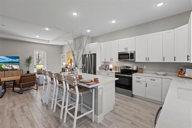 kitchen featuring stainless steel appliances, light hardwood / wood-style flooring, white cabinetry, a breakfast bar area, and an island with sink