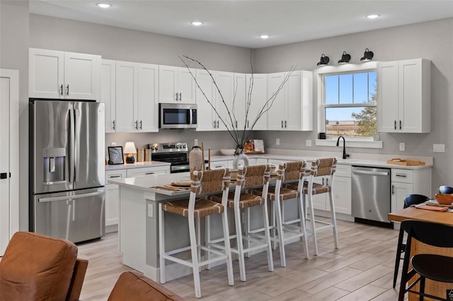 kitchen with stainless steel appliances, light hardwood / wood-style flooring, a center island, white cabinetry, and a breakfast bar area