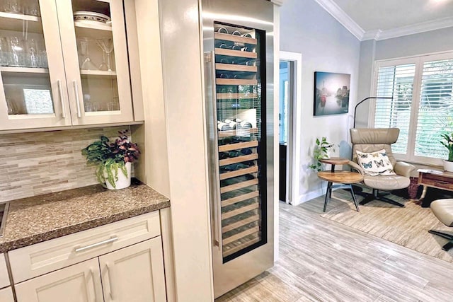 bar featuring wine cooler, ornamental molding, dark stone counters, light hardwood / wood-style floors, and decorative backsplash