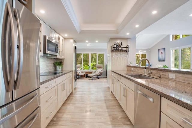 kitchen featuring sink, backsplash, stainless steel appliances, a tray ceiling, and dark stone counters