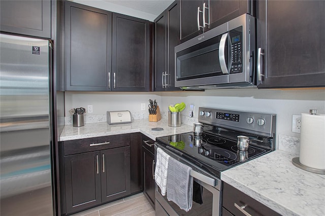 kitchen with appliances with stainless steel finishes, dark brown cabinetry, and light stone countertops