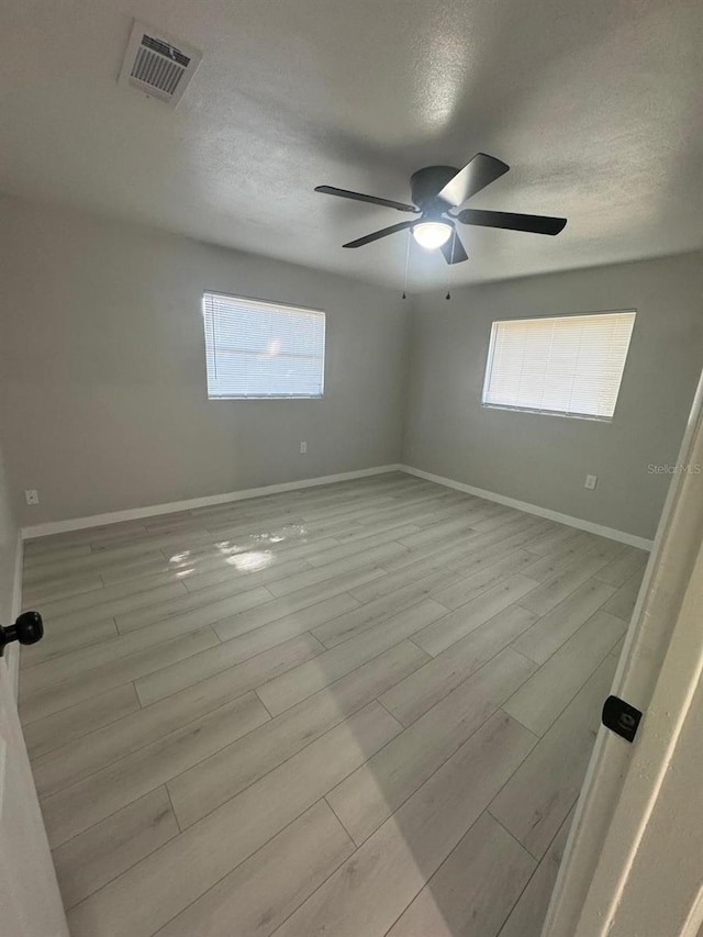 empty room featuring light hardwood / wood-style floors, a healthy amount of sunlight, ceiling fan, and a textured ceiling