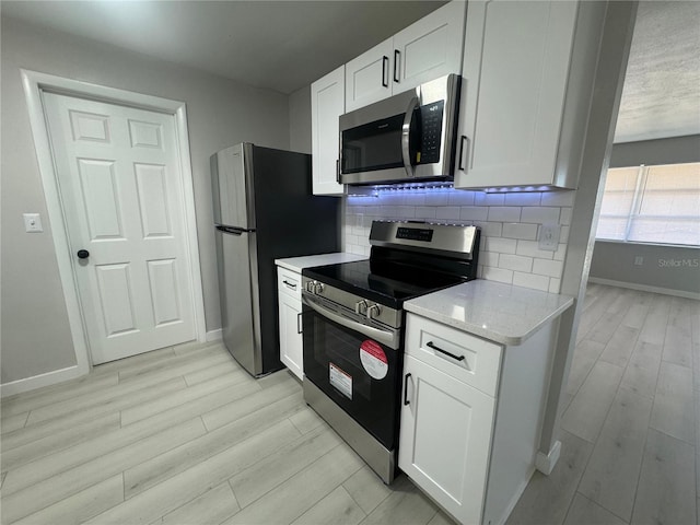 kitchen featuring backsplash, stainless steel appliances, light hardwood / wood-style floors, light stone counters, and white cabinets