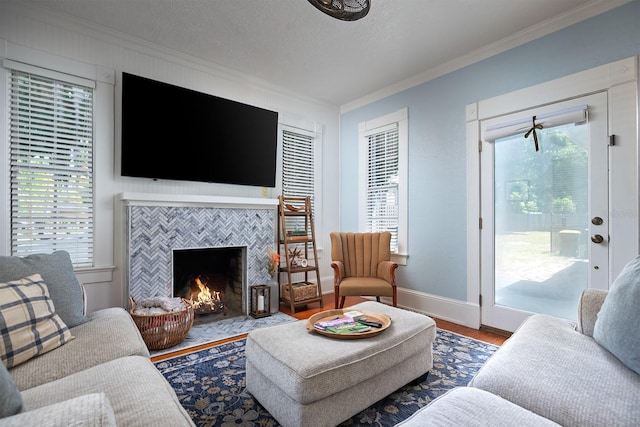 living room featuring wood-type flooring, ornamental molding, a tiled fireplace, and a healthy amount of sunlight