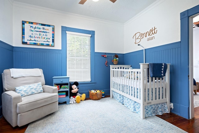 bedroom featuring ornamental molding, a nursery area, ceiling fan, and dark hardwood / wood-style floors