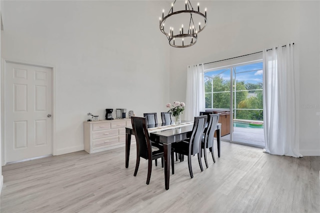 dining room with a notable chandelier, a towering ceiling, and light wood-type flooring