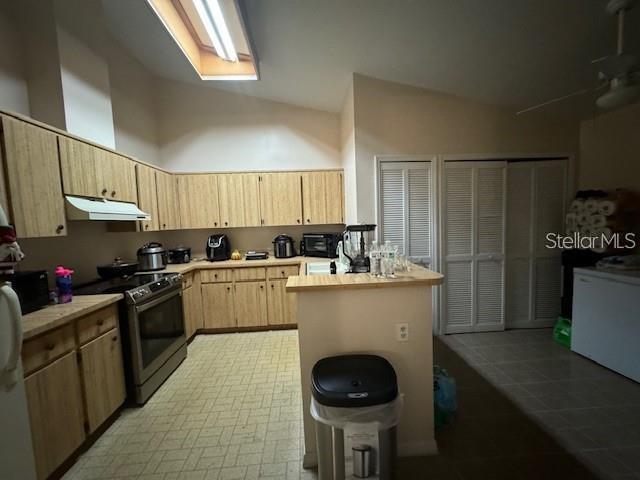 kitchen featuring a center island, high vaulted ceiling, light brown cabinets, tile floors, and electric range