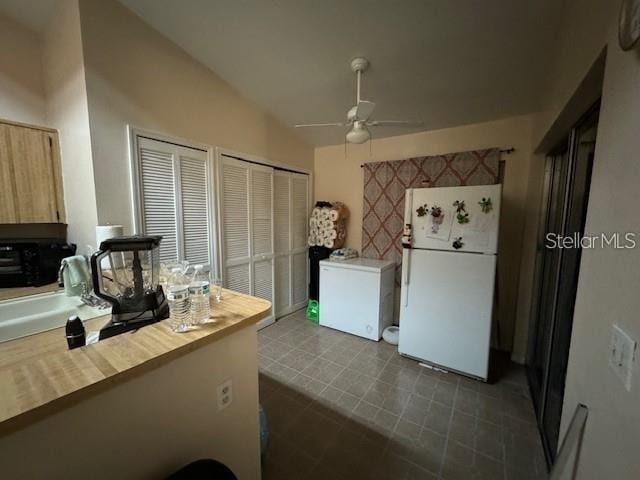 kitchen with white refrigerator, lofted ceiling, ceiling fan, and dark tile flooring