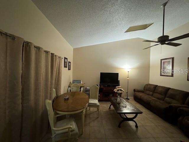 living room featuring lofted ceiling, ceiling fan, a textured ceiling, and tile flooring