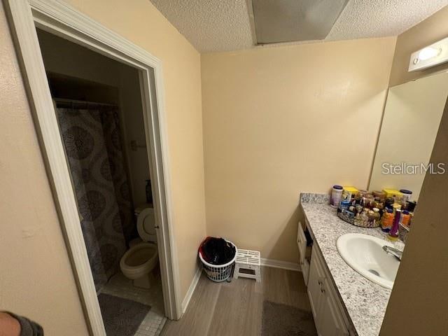 bathroom with wood-type flooring, a textured ceiling, large vanity, and toilet