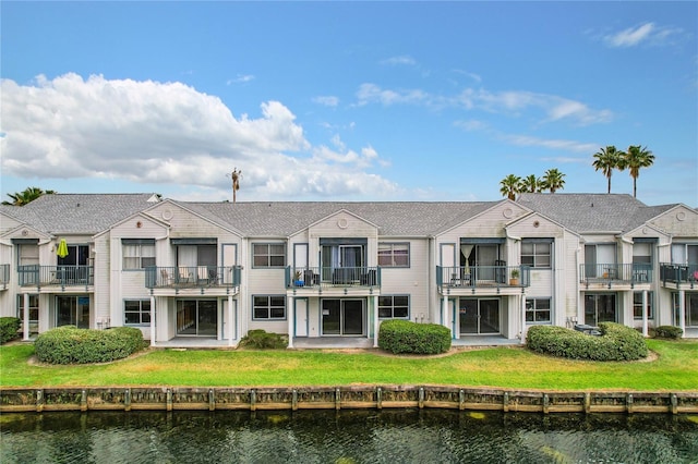 back of house featuring a balcony, a lawn, and a water view