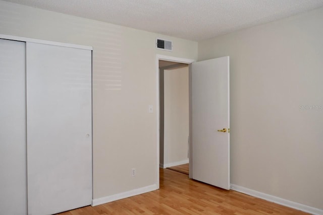 unfurnished bedroom featuring light hardwood / wood-style flooring, a closet, and a textured ceiling