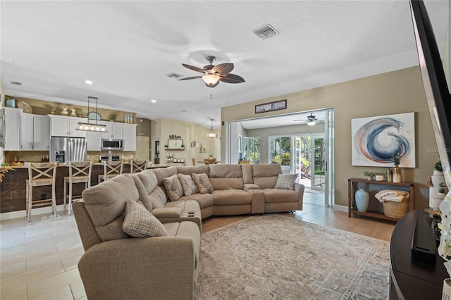 living room featuring ceiling fan, light tile flooring, and a textured ceiling