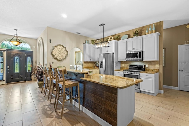 kitchen featuring a kitchen island with sink, white cabinets, light stone countertops, stainless steel appliances, and tasteful backsplash