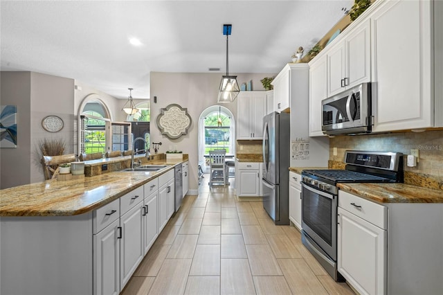 kitchen with appliances with stainless steel finishes, tasteful backsplash, white cabinetry, decorative light fixtures, and a center island with sink