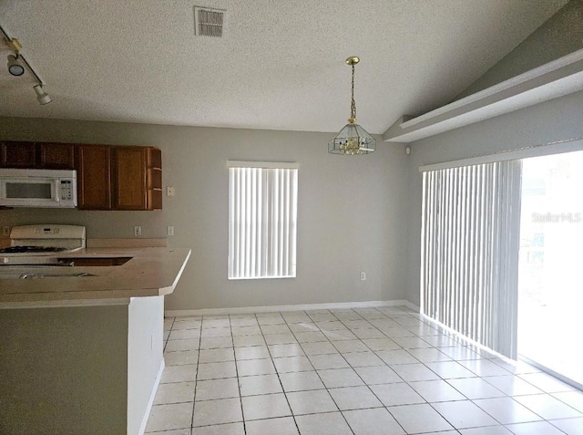 kitchen with lofted ceiling, light tile patterned floors, white appliances, a textured ceiling, and decorative light fixtures