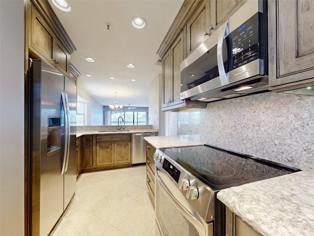 kitchen with pendant lighting, backsplash, sink, appliances with stainless steel finishes, and a notable chandelier