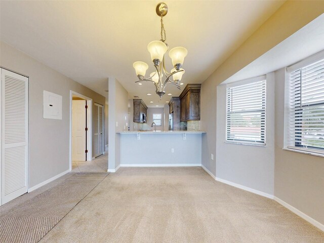 kitchen with pendant lighting, backsplash, light carpet, kitchen peninsula, and a chandelier