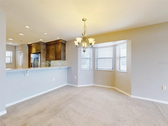 kitchen featuring decorative light fixtures, light colored carpet, kitchen peninsula, and a breakfast bar area