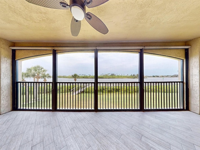 unfurnished sunroom with ceiling fan, a water view, and a healthy amount of sunlight