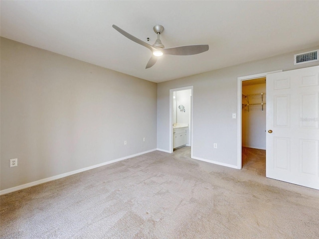 unfurnished bedroom with ensuite bathroom, ceiling fan, a spacious closet, light colored carpet, and a closet