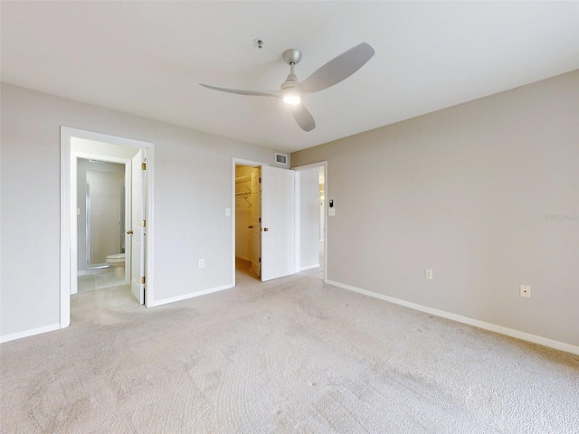 unfurnished bedroom with ceiling fan, ensuite bathroom, light colored carpet, a walk in closet, and a closet