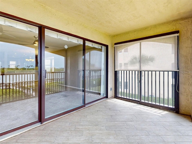 unfurnished sunroom featuring ceiling fan and plenty of natural light