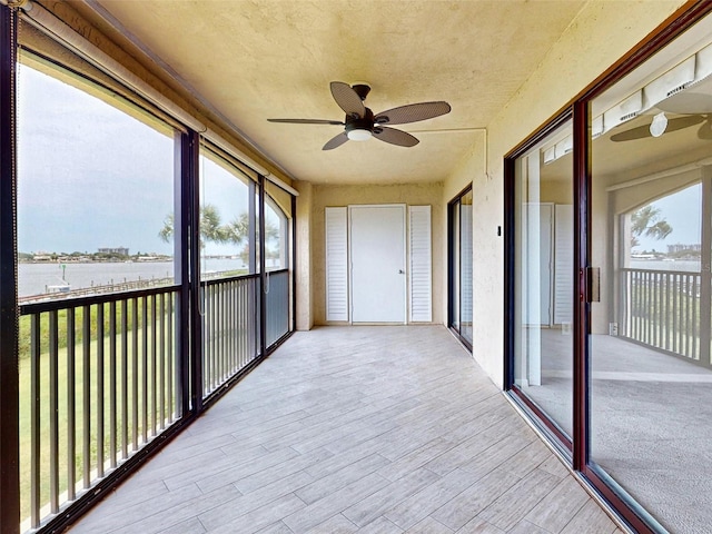 unfurnished sunroom with ceiling fan and a water view