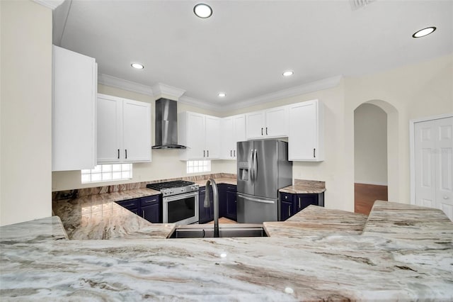 kitchen with white cabinetry, wall chimney range hood, stainless steel appliances, blue cabinetry, and sink